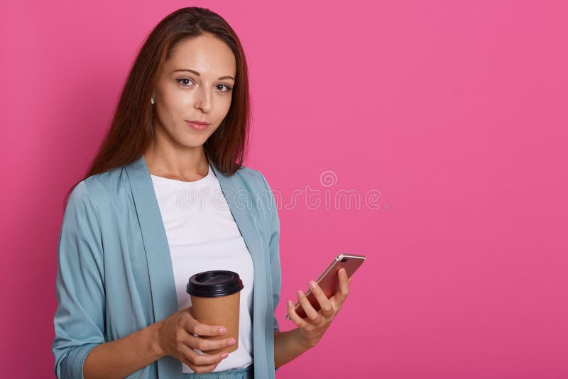 Image of young european woman with staraight hair holding mobile phone and takeaway coffee in paper cup, model posing isolated stock photography Image of young european woman with staraight hair holding mobile phone and takeaway coffee in paper cup, model posing isolated stock photography
