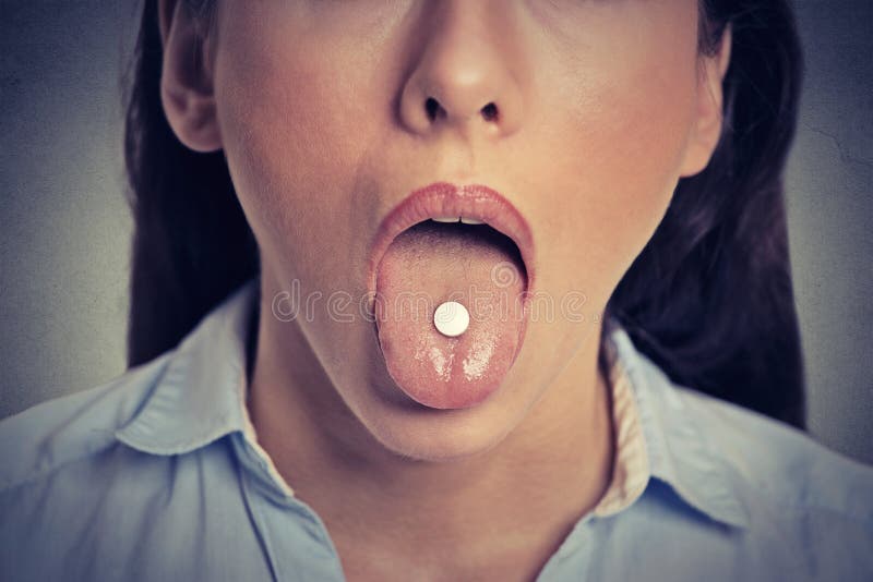 Imagem colhida da jovem mulher com o comprimido branco em sua língua