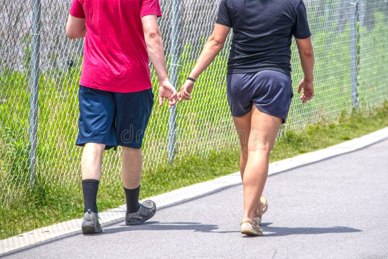 Imagem colhida de dois adultos novos que vestem o short e os t-shirt na fuga de passeio pavimentada com os dedos entrela?ados - c fotos de stock Imagem colhida de dois adultos novos que vestem o short e os t-shirt na fuga de passeio pavimentada com os dedos entrela?ados - c fotos de stock