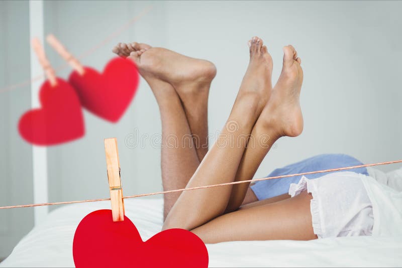 Imagem composta de corações vermelhos e dos pares de suspensão que encontram-se na cama com pé cruzado fotografia de stock Imagem composta de corações vermelhos e dos pares de suspensão que encontram-se na cama com pé cruzado fotografia de stock