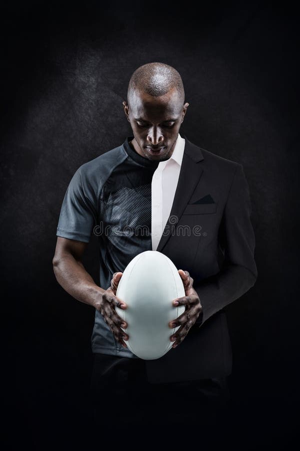 Imagem composta do atleta pensativo que olha a bola de rugby fotografia de stock royalty free Imagem composta do atleta pensativo que olha a bola de rugby fotografia de stock royalty free
