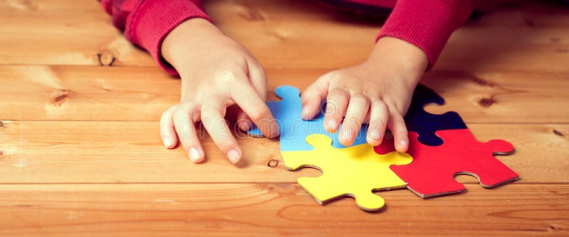 Imagem de faixa das mãos de uma criança autista tocando um símbolo de puzzle da consciência pública para o autismo