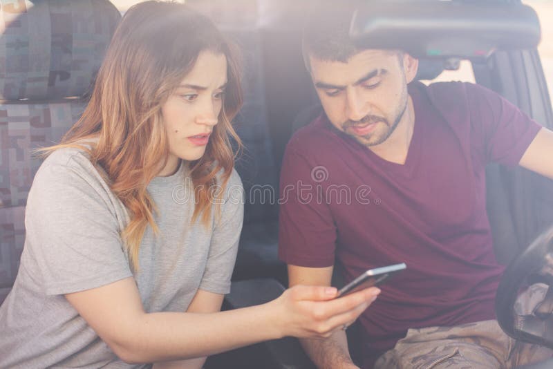 A imagem de olhares concentrados dos pares no telefone celular, quando em linha video do relógio que está no engarrafamento, sent imagem de stock royalty free A imagem de olhares concentrados dos pares no telefone celular, quando em linha video do relógio que está no engarrafamento, sent imagem de stock royalty free