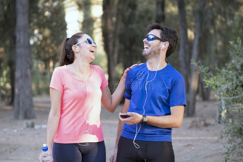 Imagem de um homem e mulher entusiasmados com fones de ouvido ouvindo música em celulares no parque imagem de stock royalty free Imagem de um homem e mulher entusiasmados com fones de ouvido ouvindo música em celulares no parque imagem de stock royalty free
