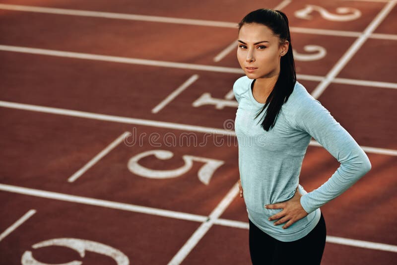 Imagem horizontal ao ar livre de uma jovem atleta que se posiciona em pista de corrida no estádio Retrato de um belo desportista foto de stock Imagem horizontal ao ar livre de uma jovem atleta que se posiciona em pista de corrida no estádio Retrato de um belo desportista foto de stock