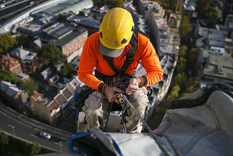 Imagen ascendente cercana del trabajador de sexo masculino de los trabajos del acceso de la cuerda que lleva el casco amarillo, c foto de archivo Imagen ascendente cercana del trabajador de sexo masculino de los trabajos del acceso de la cuerda que lleva el casco amarillo, c foto de archivo