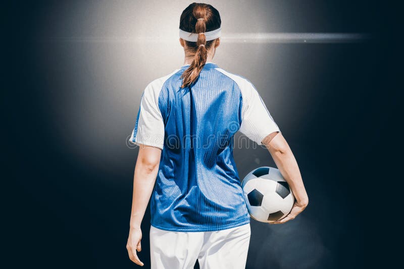 Imagen compuesta de la vista posterior del jugador de fútbol de la mujer que sostiene una bola imagen de archivo libre de regalías Imagen compuesta de la vista posterior del jugador de fútbol de la mujer que sostiene una bola imagen de archivo libre de regalías