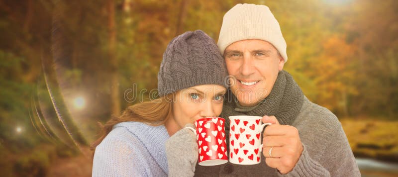 Imagen compuesta de pares felices en la ropa caliente que sostiene las tazas