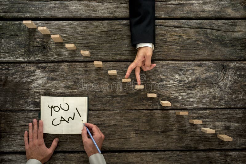 Conceptual image of personal growth and career development with businessman walking his fingers up wooden steps while his colleague or mentor encourages him with a You can message. Conceptual image of personal growth and career development with businessman walking his fingers up wooden steps while his colleague or mentor encourages him with a You can message.