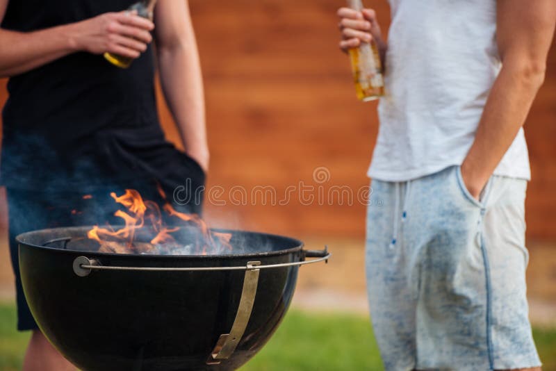 Imagen cosechada de dos hombres que sostienen las botellas de cerveza mientras que barbacoa imagen de archivo Imagen cosechada de dos hombres que sostienen las botellas de cerveza mientras que barbacoa imagen de archivo