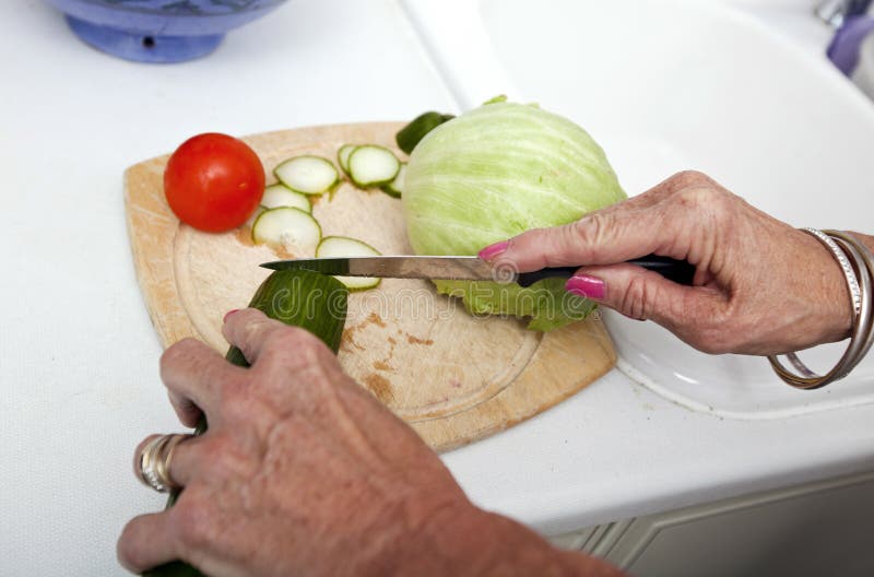Imagen cosechada de la mujer mayor que taja verduras en tabla de cortar en cocina