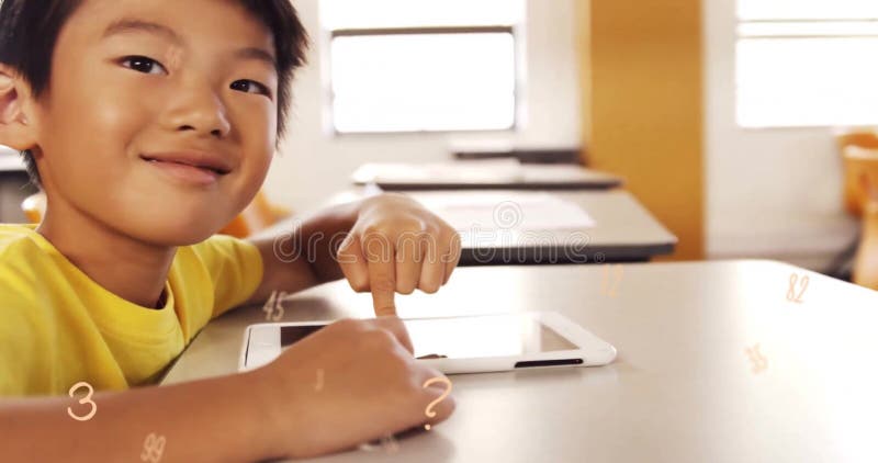 Imagen de múltiples números sobre cerca de un niño asiático sonriente usando una tableta digital en el aula foto de archivo libre de regalías