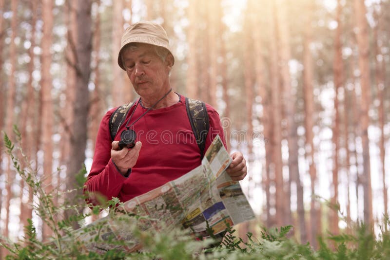 Imagen del hombre del eldery que camina y que mira el compás y el mapa para la dirección para el viaje en el bosque, equipo casua fotos de archivo Imagen del hombre del eldery que camina y que mira el compás y el mapa para la dirección para el viaje en el bosque, equipo casua fotos de archivo