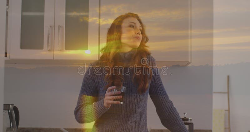 Imagen del paisaje de la puesta del sol sobre una mujer caucásica tomando café en la cocina fotos de archivo