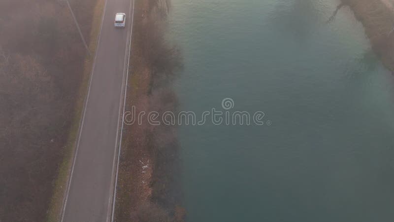 Images aériennes d'une voiture blanche conduisant sur une route asphaltée étroite près d'une rivière en automne banque de vidéos