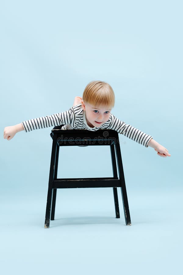 Imaginative blond boy lying on stepping stool with arms spread apart like wings