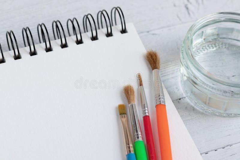 Imballaggio per l'arte, spazzole per vernici e vetro d'acqua su una superficie di legno Desk artistico con una profondità di camp immagine stock Imballaggio per l'arte, spazzole per vernici e vetro d'acqua su una superficie di legno Desk artistico con una profondità di camp immagine stock