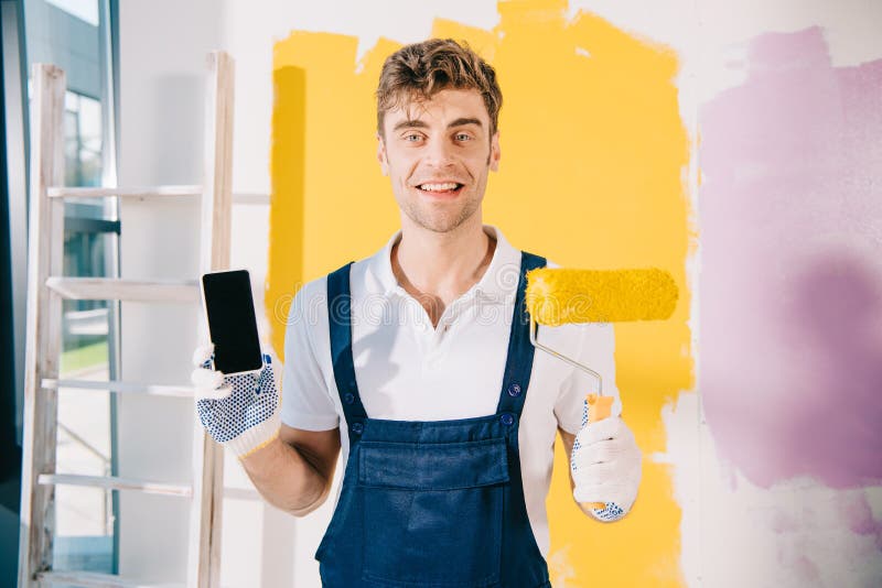Imbianchino in uniforme che tiene in mano uno smartphone fotografia stock