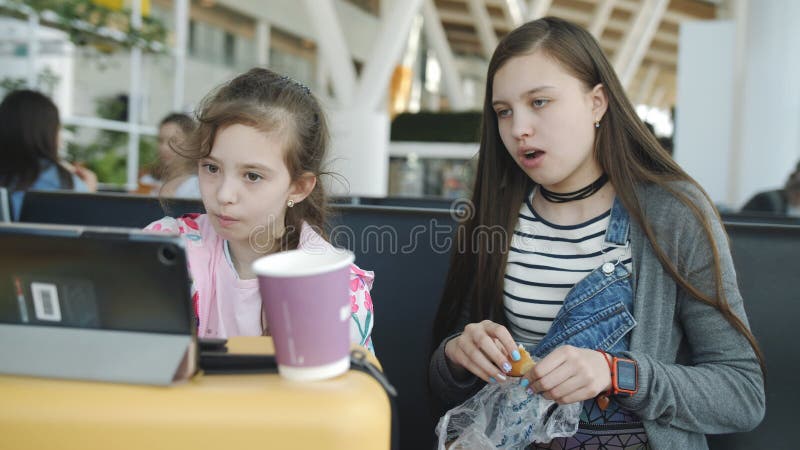 Imbiss am Flughafen. zwei Schwestern sehen sich Zeichentrickfilme auf der Tablette an und trinken Tee mit Keksen.