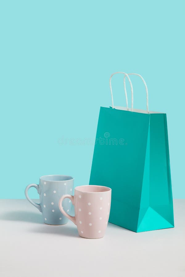 Immagine alta falsa con la tendenza delle tazze del t? vicino al supporto del sacco di carta su fondo blu Immagine di concetto de immagine stock libera da diritti Immagine alta falsa con la tendenza delle tazze del t? vicino al supporto del sacco di carta su fondo blu Immagine di concetto de immagine stock libera da diritti