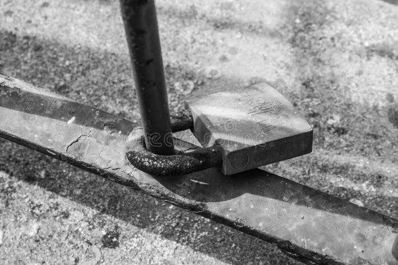 Immagine in bianco e nero di un lucchetto legato a un palo arrugginito fotografia stock