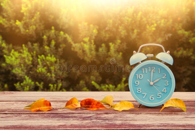 Immagine del cambiamento di tempo di autunno Regredisce il concetto Asciughi le foglie e la sveglia d'annata sulla tavola di legn