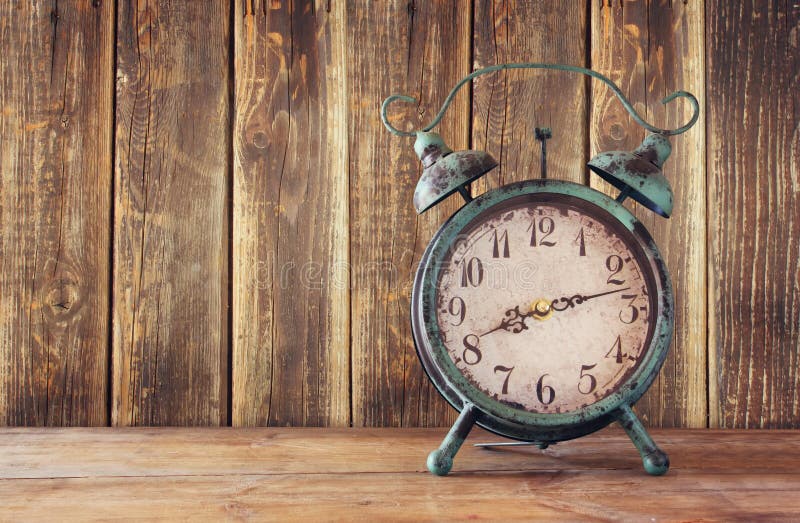 Image of vintage alarm clock on wooden table in front of wooden background. retro filtered. Image of vintage alarm clock on wooden table in front of wooden background. retro filtered.