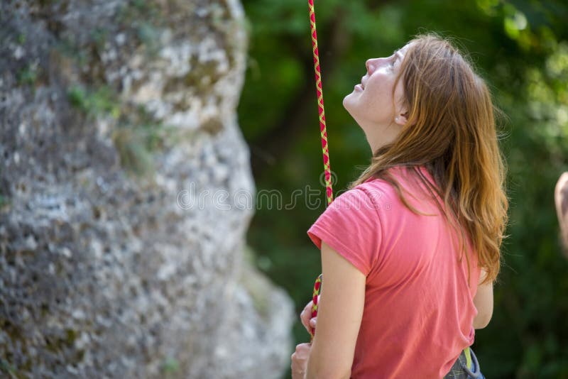 Immagine dello scalatore della giovane donna con la corda di sicurezza in mani di roccia su fondo degli alberi verdi