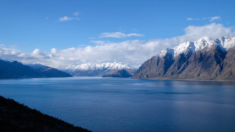 Immagine di viaggio della Nuova Zelanda del lago Hawea con la montagna della neve ed il lago blu dello specchio fotografia stock libera da diritti Immagine di viaggio della Nuova Zelanda del lago Hawea con la montagna della neve ed il lago blu dello specchio fotografia stock libera da diritti