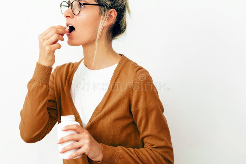 Immagine orizzontale da studio di una giovane donna vestita in modo casuale e con occhiali che prende una pillola con olio omega- fotografie stock Immagine orizzontale da studio di una giovane donna vestita in modo casuale e con occhiali che prende una pillola con olio omega- fotografie stock