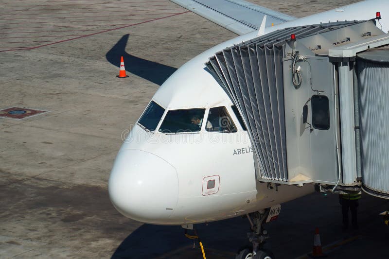 Immagine orizzontale del pilota in cabina di pilotaggio di un jet bianco parcheggiato collegato a un ponte di imbarco passeggeri. fotografie stock