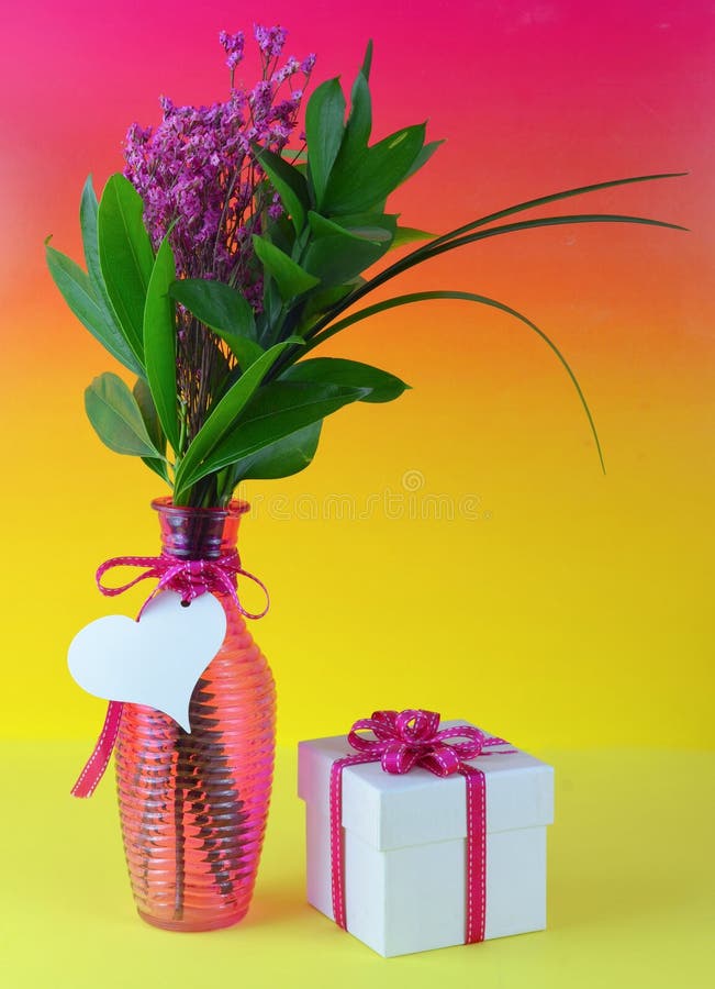 Immagine variopinta dei fiori secchi rosa con le grandi foglie verdi in un vaso rosa costolato Una carta a forma di del cuore è l immagine stock Immagine variopinta dei fiori secchi rosa con le grandi foglie verdi in un vaso rosa costolato Una carta a forma di del cuore è l immagine stock