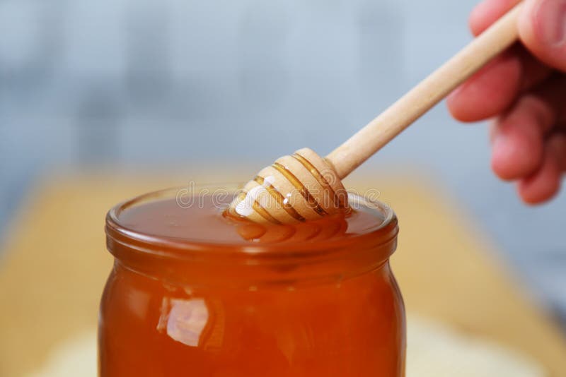 A person`s hand holds a honey spoon. Dips a ladle into a jar of honey. Glass jar filled with bee honey. Close-up view. Sweet food. A person`s hand holds a honey spoon. Dips a ladle into a jar of honey. Glass jar filled with bee honey. Close-up view. Sweet food