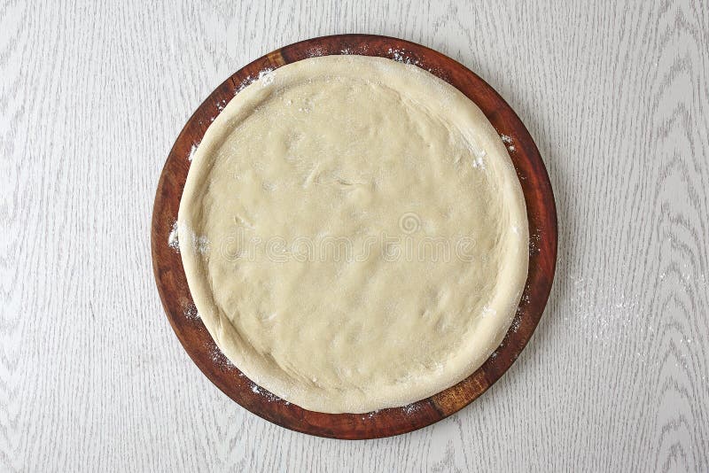 Pizza dough, 2nd step of spread the pizza dough on wooden board  on gray background. How to make Pizza? The basics of pizza making process, top view, top shot. Pizza dough, 2nd step of spread the pizza dough on wooden board  on gray background. How to make Pizza? The basics of pizza making process, top view, top shot