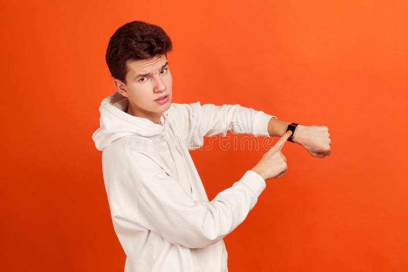Impatient young man in stylish white sweatshirt with serious face pointing his finger on handwatch, time to act, deadline