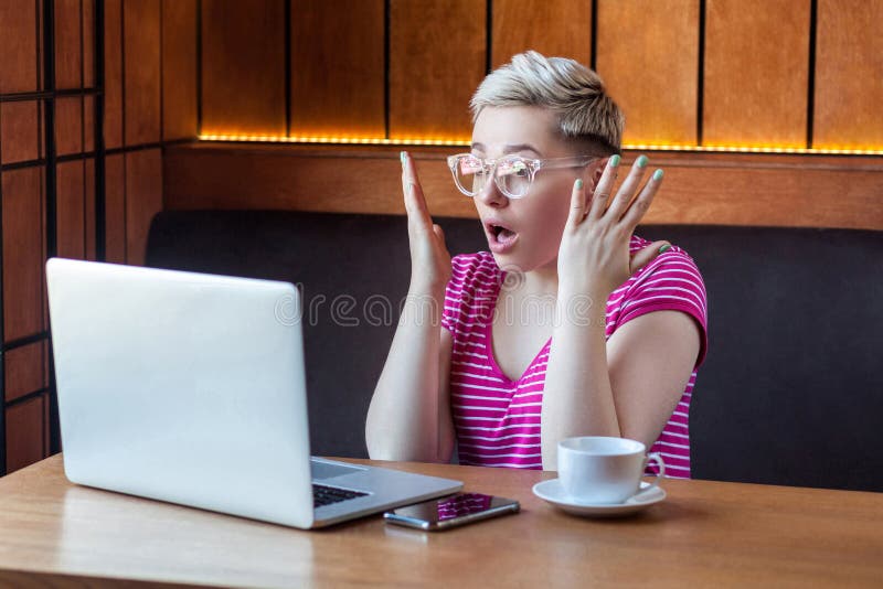 Impossible! Portrait d'une jeune fille incroyable aux cheveux courts en t-shirt rose et lunettes est assise dans un café, travai photo stock