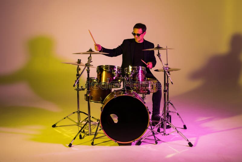 Caucasian male drummer improvising isolated on light studio background in neon light. Performing, looks inspired, energy. Caucasian male drummer improvising isolated on light studio background in neon light. Performing, looks inspired, energy