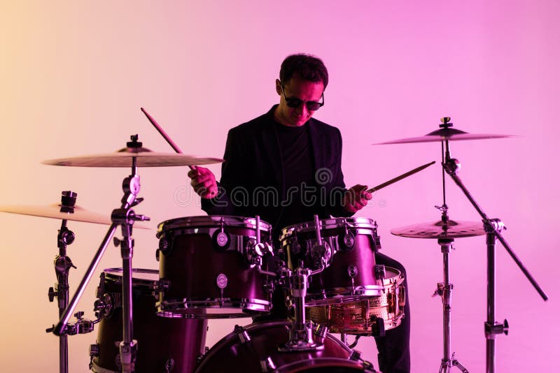 Caucasian male drummer improvising isolated on light studio background in neon light. Performing, looks inspired, energy. Caucasian male drummer improvising isolated on light studio background in neon light. Performing, looks inspired, energy