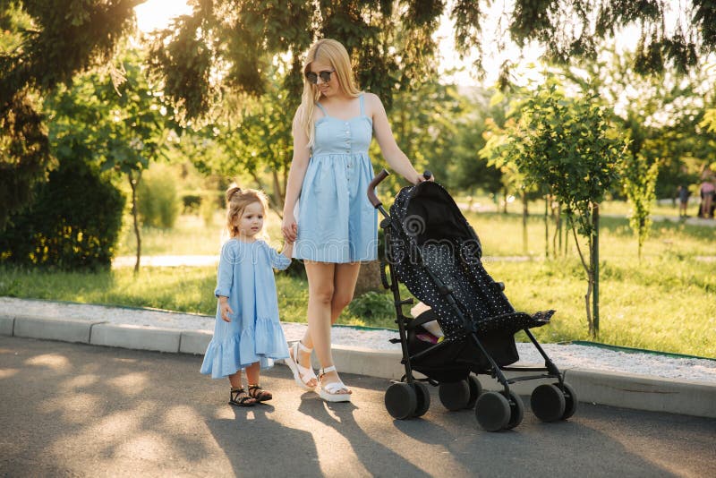 Impulso pequeno da mam? das ajudas da filha o transporte de beb? imagem de stock Impulso pequeno da mam? das ajudas da filha o transporte de beb? imagem de stock
