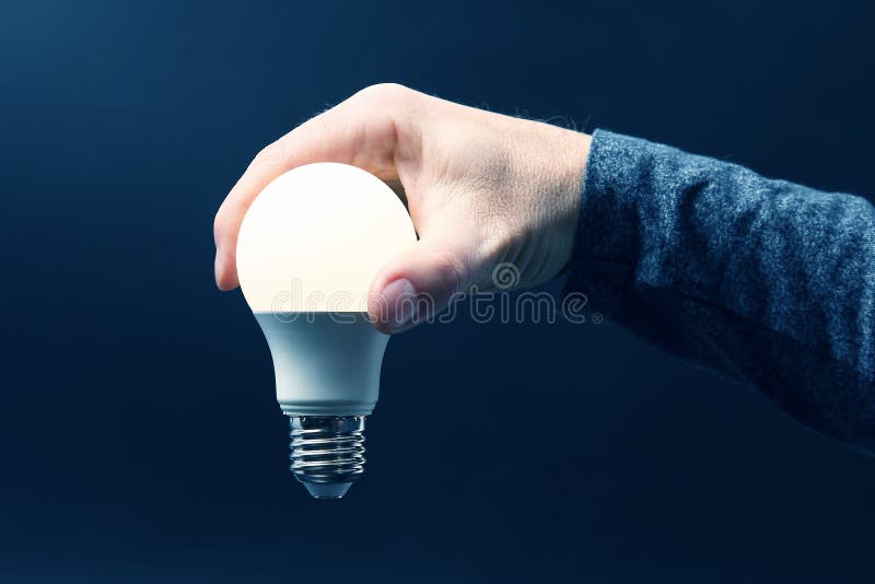 Inbegrepen geleide lamp in menselijke hand op donkerblauwe achtergrond royalty-vrije stock afbeelding Inbegrepen geleide lamp in menselijke hand op donkerblauwe achtergrond royalty-vrije stock afbeelding