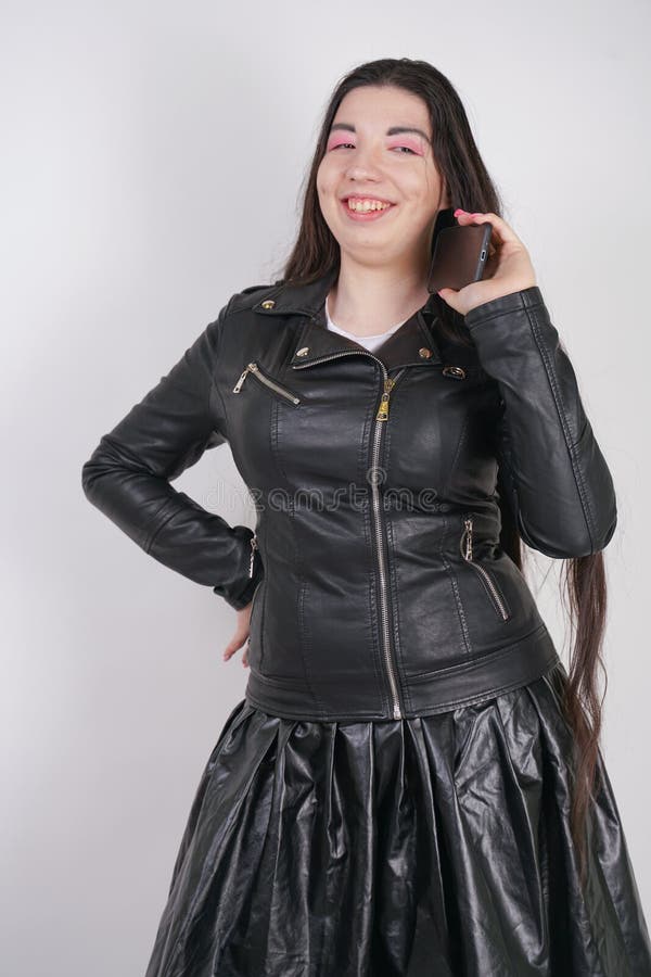 Incantare castana in bomber nero nei supporti di stile della roccia con uno smartphone su un fondo bianco nello studio fotografia stock