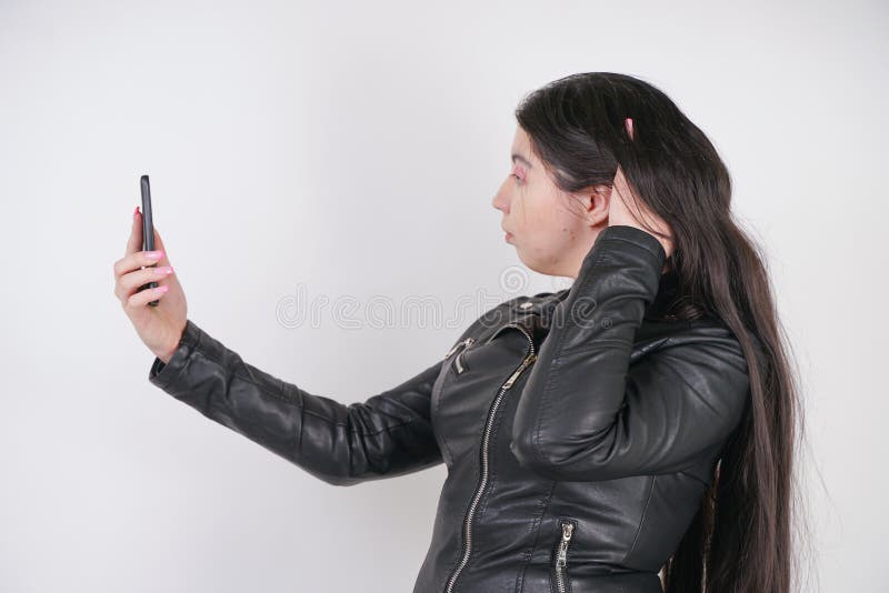 Incantare castana in bomber nero nei supporti di stile della roccia con uno smartphone su un fondo bianco nello studio fotografie stock