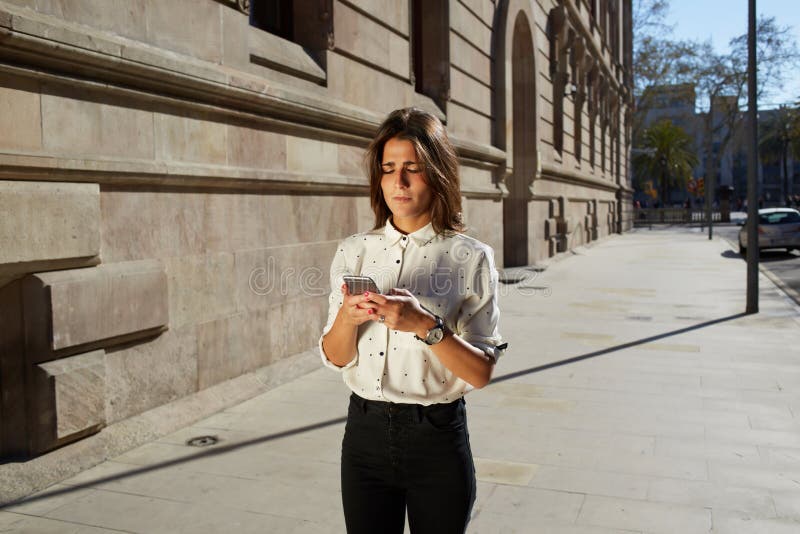 Inconformista femenino elegante que usa su teléfono móvil mientras que camina en el ambiente urbano con el área de espacio grande fotos de archivo Inconformista femenino elegante que usa su teléfono móvil mientras que camina en el ambiente urbano con el área de espacio grande fotos de archivo