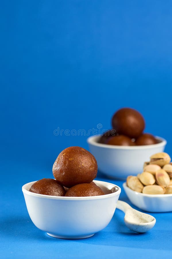 Indian Dessert Gulab Jamun in Bowl with Spoon on Blue Background
