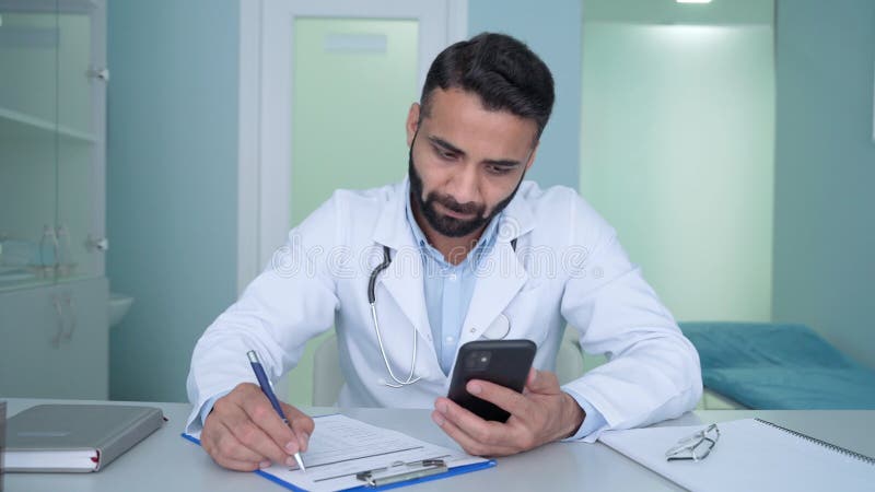 Indian male doctor in hospital clinic uses cell mobile phone apps, texting.