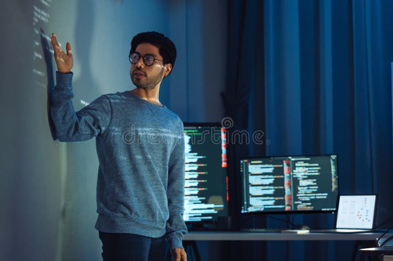 Indian man programmer standing in front of a screen with code projected presentation the integration of technology and human royalty free stock image