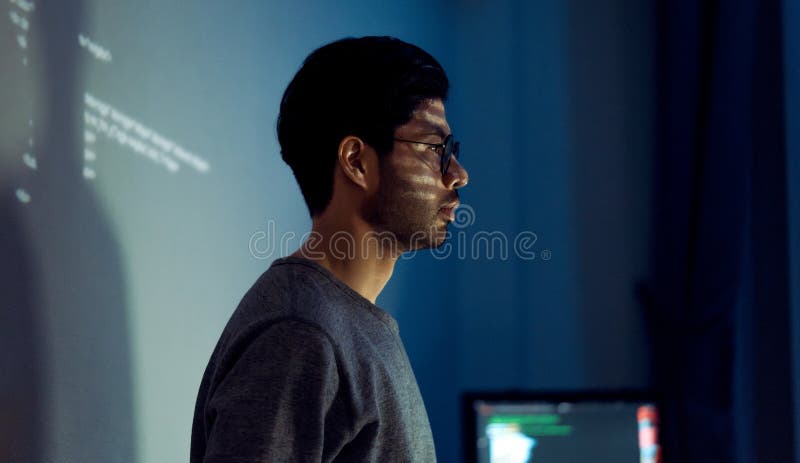 Indian man programmer standing in front of a screen with code projected presentation the integration of technology and human stock images