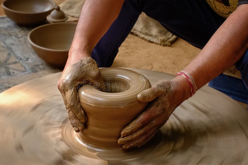 Pottery - skilled wet hands of potter shaping the clay on potter wheel. Pot, vase throwing. Manufacturing traditional handicraft Indian bowl, jar, pot, jug. Shilpagram, Udaipur, Rajasthan, India. Pottery - skilled wet hands of potter shaping the clay on potter wheel. Pot, vase throwing. Manufacturing traditional handicraft Indian bowl, jar, pot, jug. Shilpagram, Udaipur, Rajasthan, India