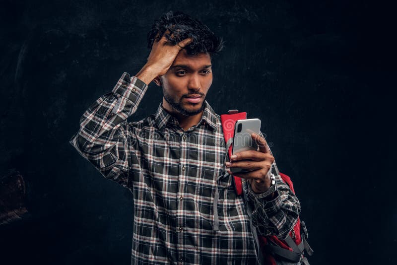 Indian student with a backpack forgot about something very important and with a frustrated look looks at his smartphone. royalty free stock images Indian student with a backpack forgot about something very important and with a frustrated look looks at his smartphone. royalty free stock images