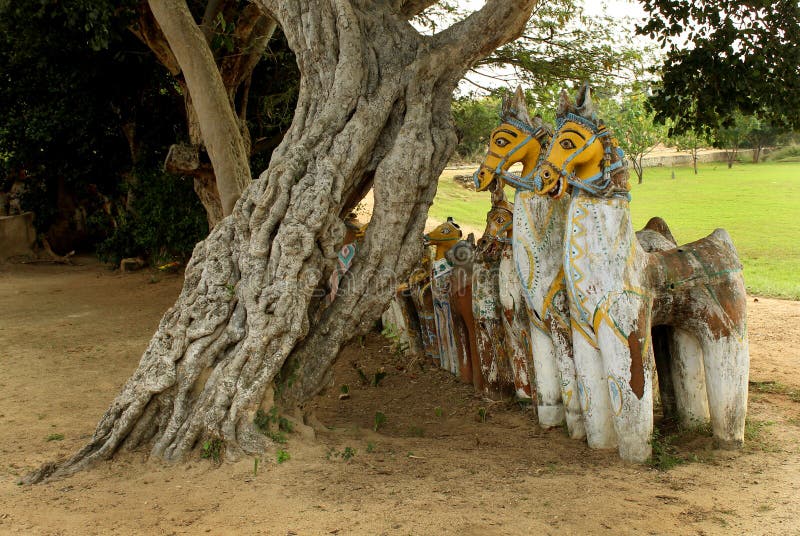 Indian village god of horse statues with old tree at a village temple complex.